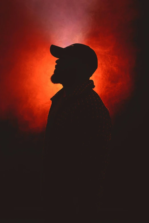 a silhouette s of a man wearing a hat in front of some red light