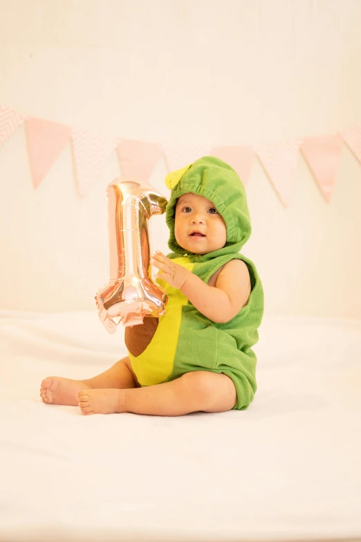 a baby with a silver balloon in a green costume