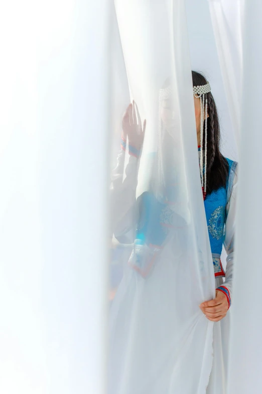 a woman is looking out from behind the white curtains