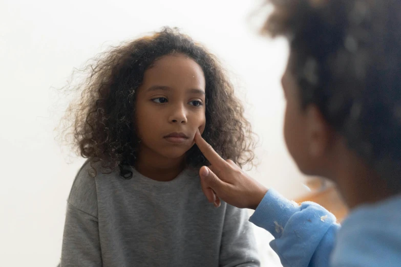 a  combs her hair while someone in a blue sweater sits at a table