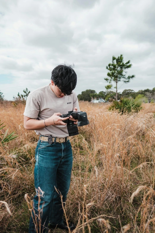 a boy stands in tall grass with an old camera