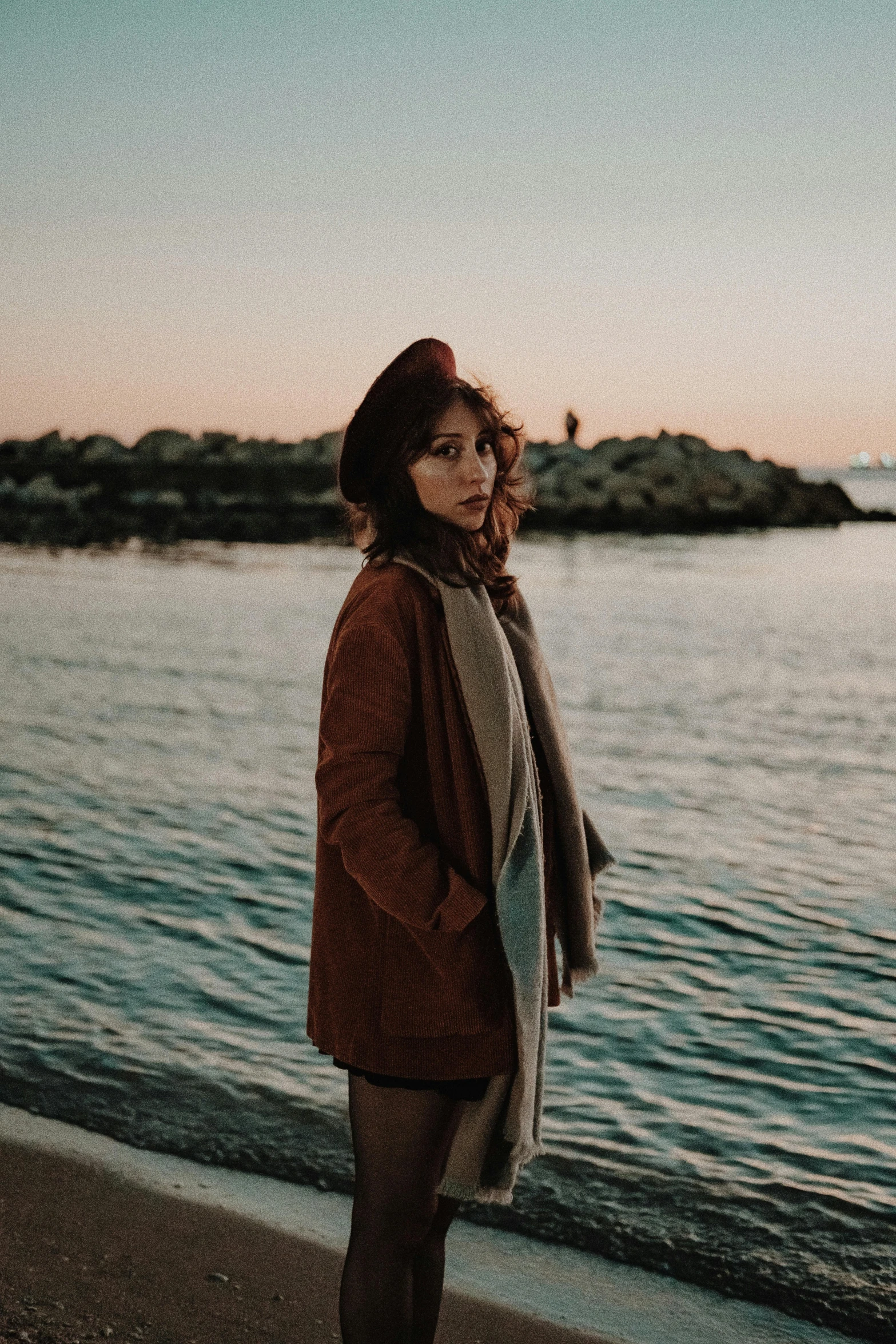 woman with brown hat and coat standing on edge of water