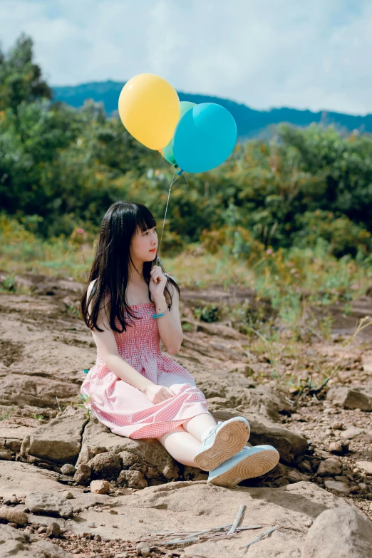 a girl sitting on the ground holding two balloons