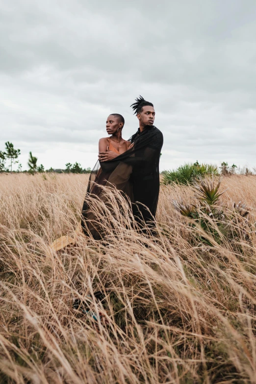 two people posing in tall dry grass on an overcast day