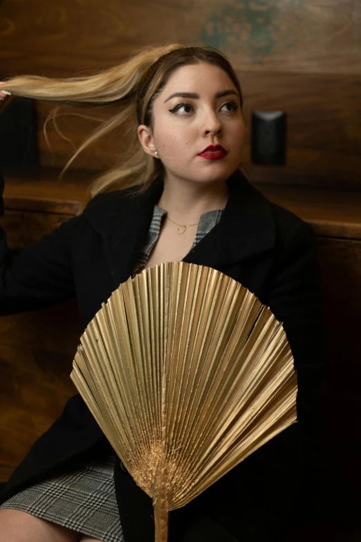 woman in black coat with gold fan posing for camera