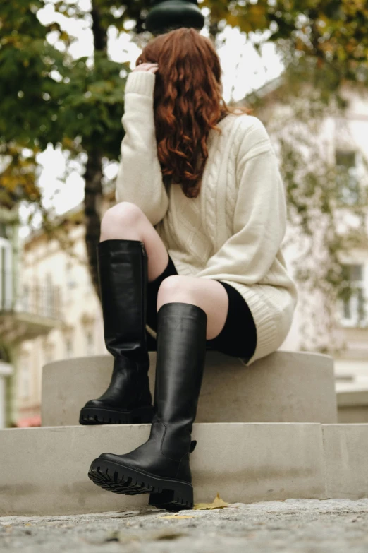 a woman in knee high boots is sitting on concrete