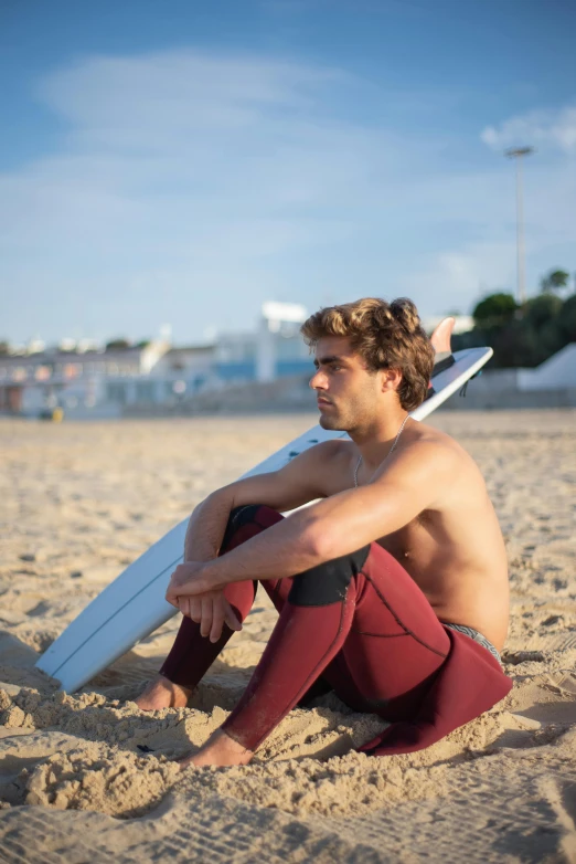 a shirtless man sitting on the sand with his surf board