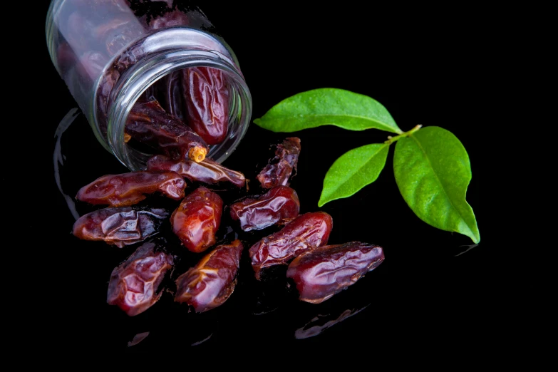 the small bottle contains red fruit and sits next to a leaf