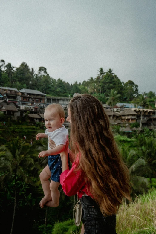 a woman holding a baby next to a forest