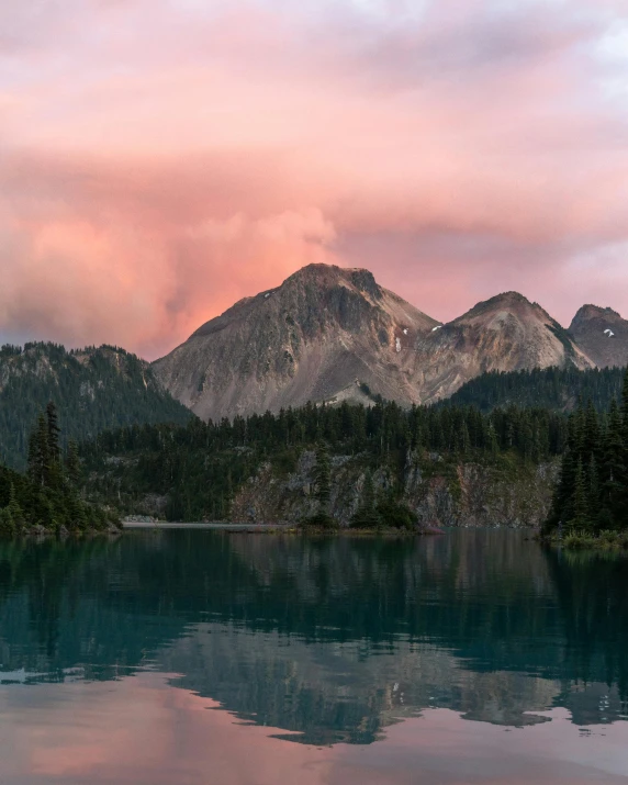 some mountains with trees are reflected in a calm lake