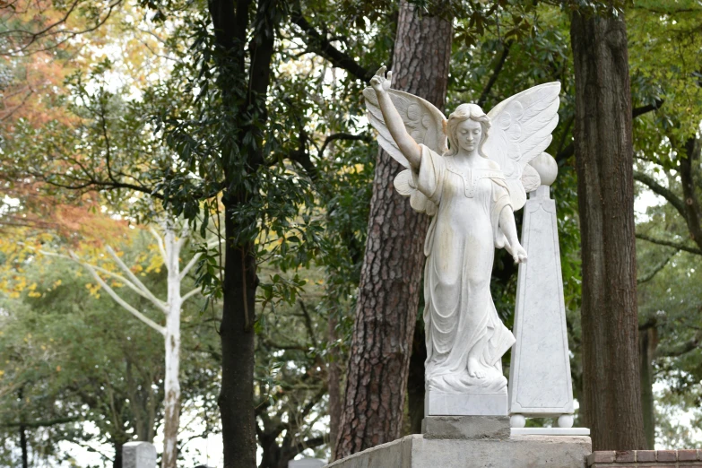 white angel statue sitting next to two graves