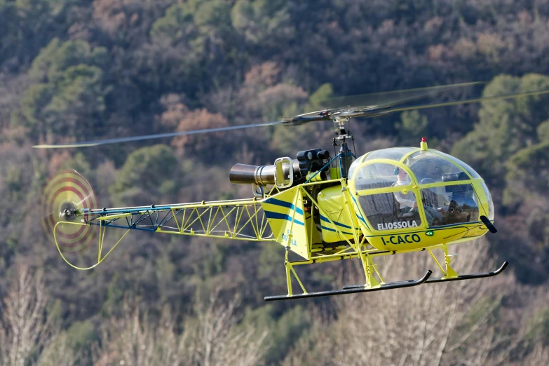 a man in a yellow helicopter near a forest