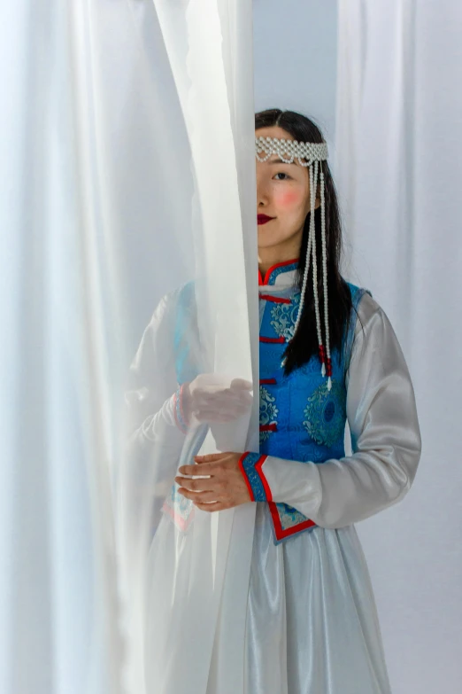 a woman in a white and blue dress is hiding behind curtains