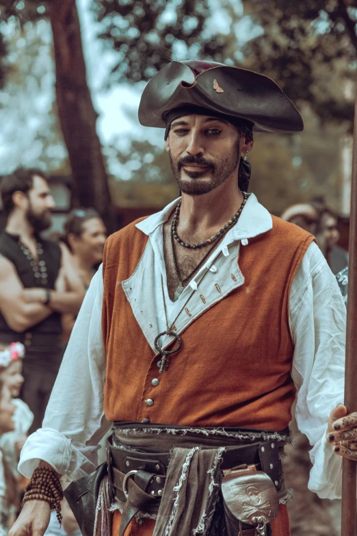 a man wearing a large hat stands holding a wooden stick