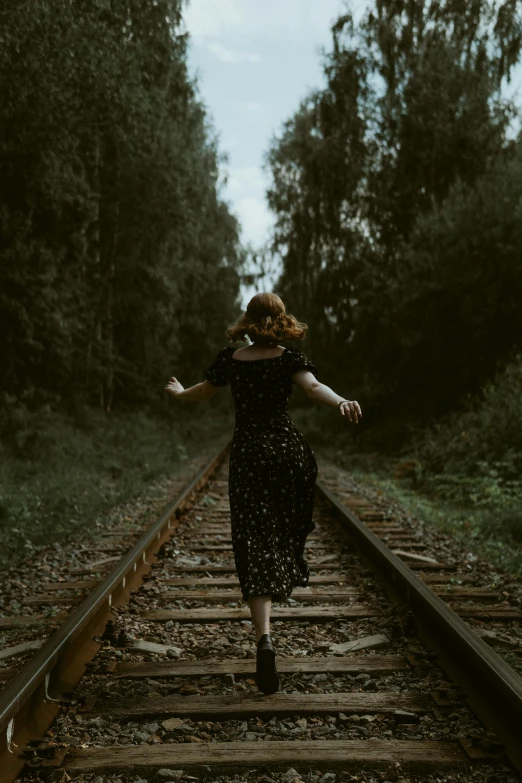 a woman in a black dress runs on railroad tracks