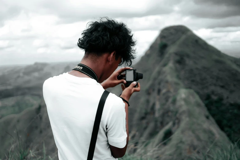 a person holding a camera taking a picture with a mountain behind them