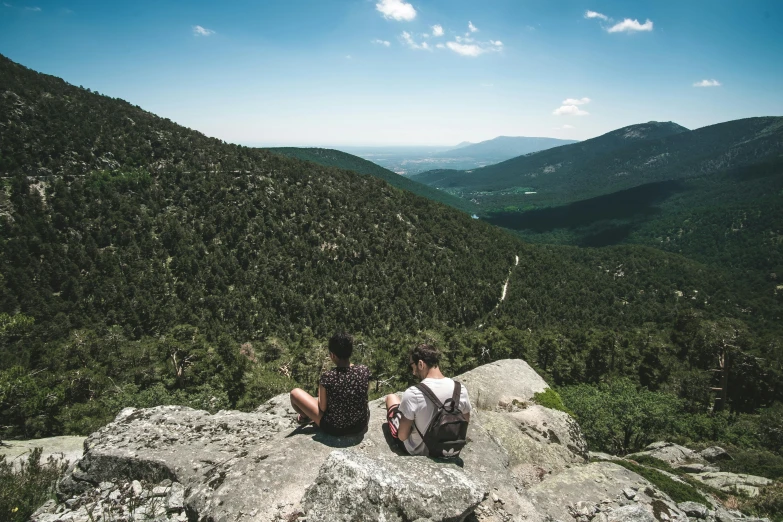 two people are sitting on a hill overlooking mountains