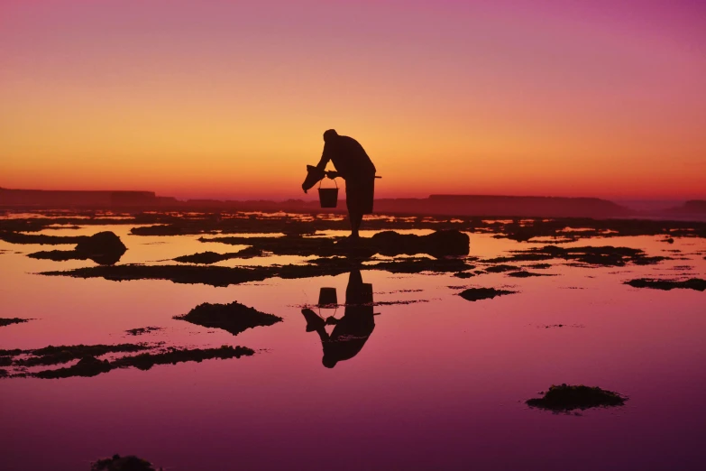 a person is throwing rocks into the water at sunset