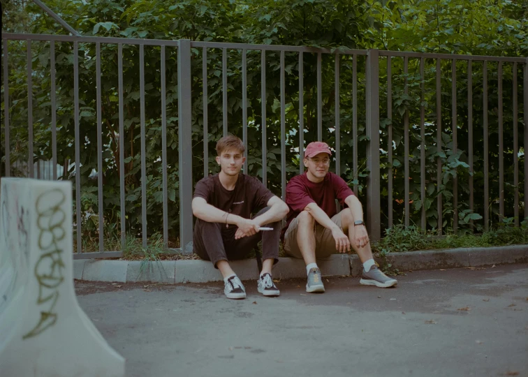 two boys sitting on the edge of an outdoor skateboard park