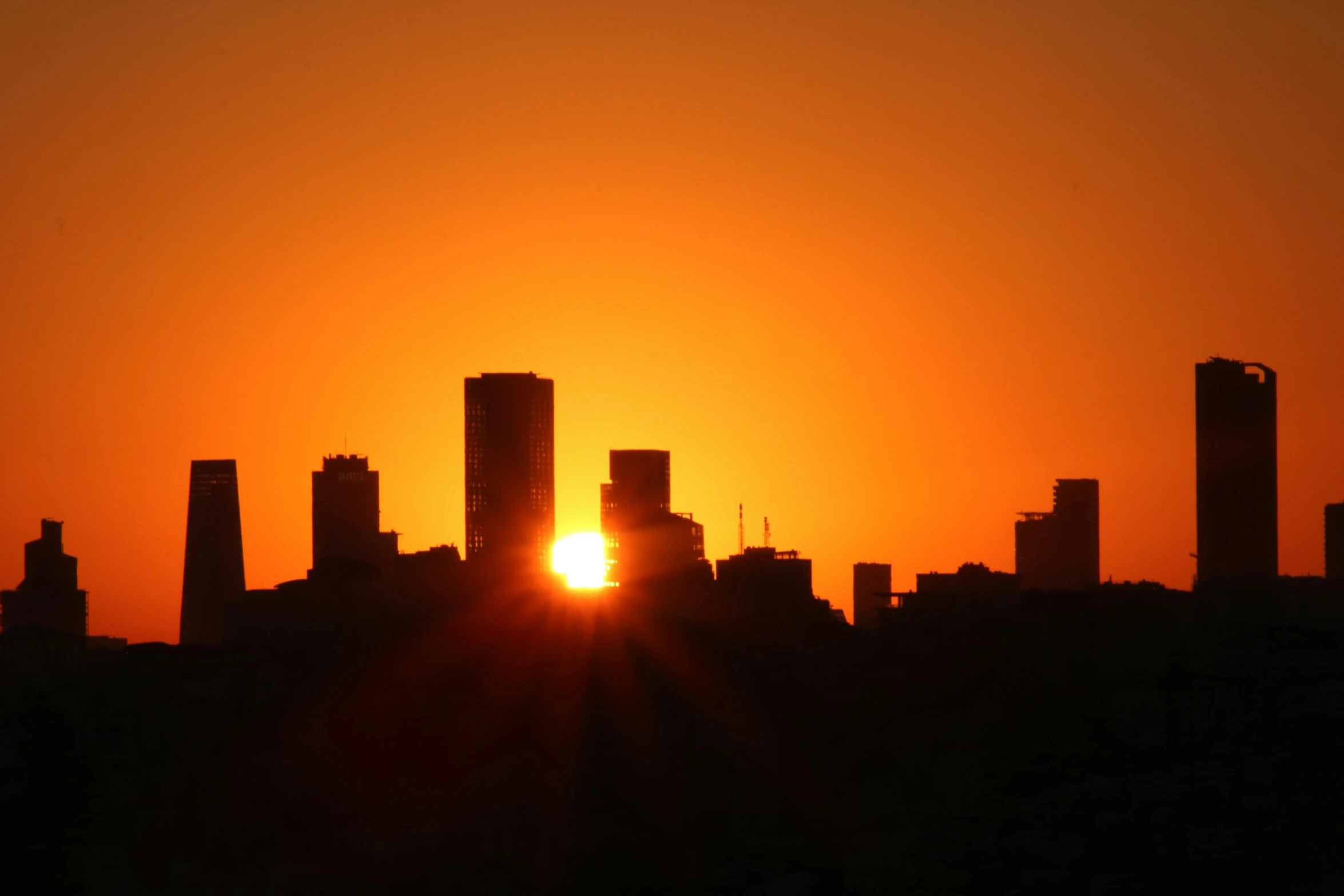 the sun setting behind an apartment building silhouetted by a city