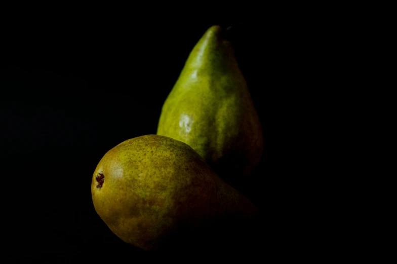 there is a green pear and two other pears in a black room