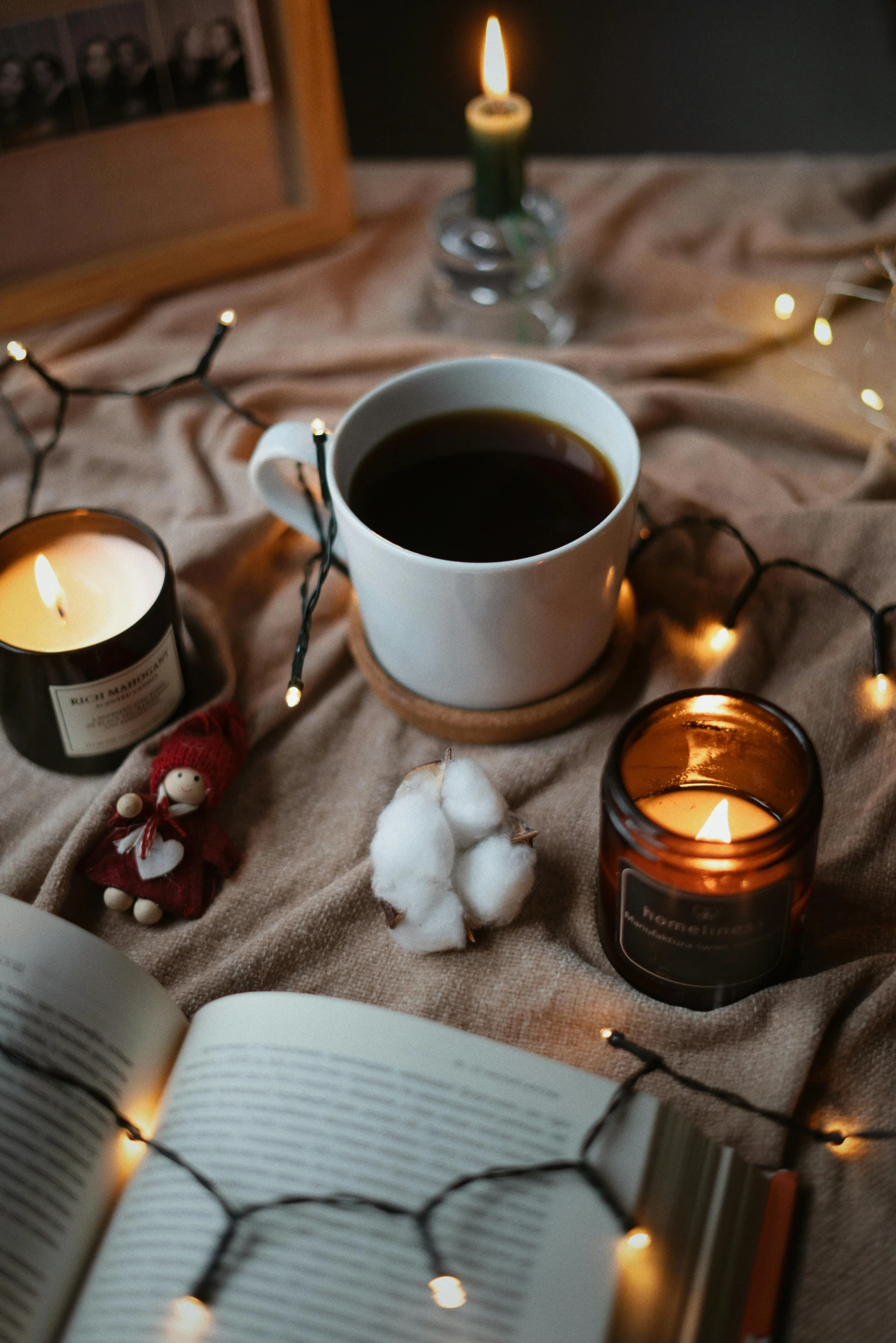 a cup of coffee, candles, and an open book on a table