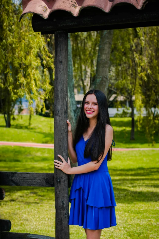 a beautiful young woman wearing a blue dress standing by a gazebo