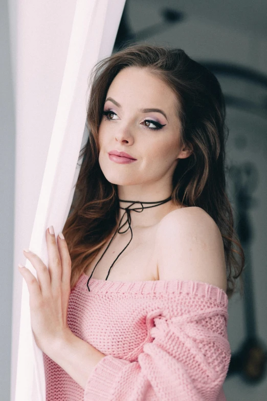 a girl posing with a pink top while looking out a window