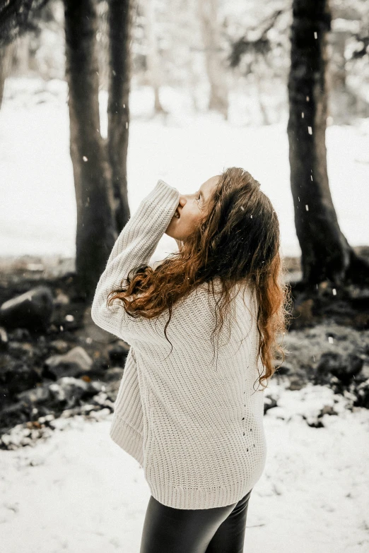 a girl in the woods looking up at trees covered in snow