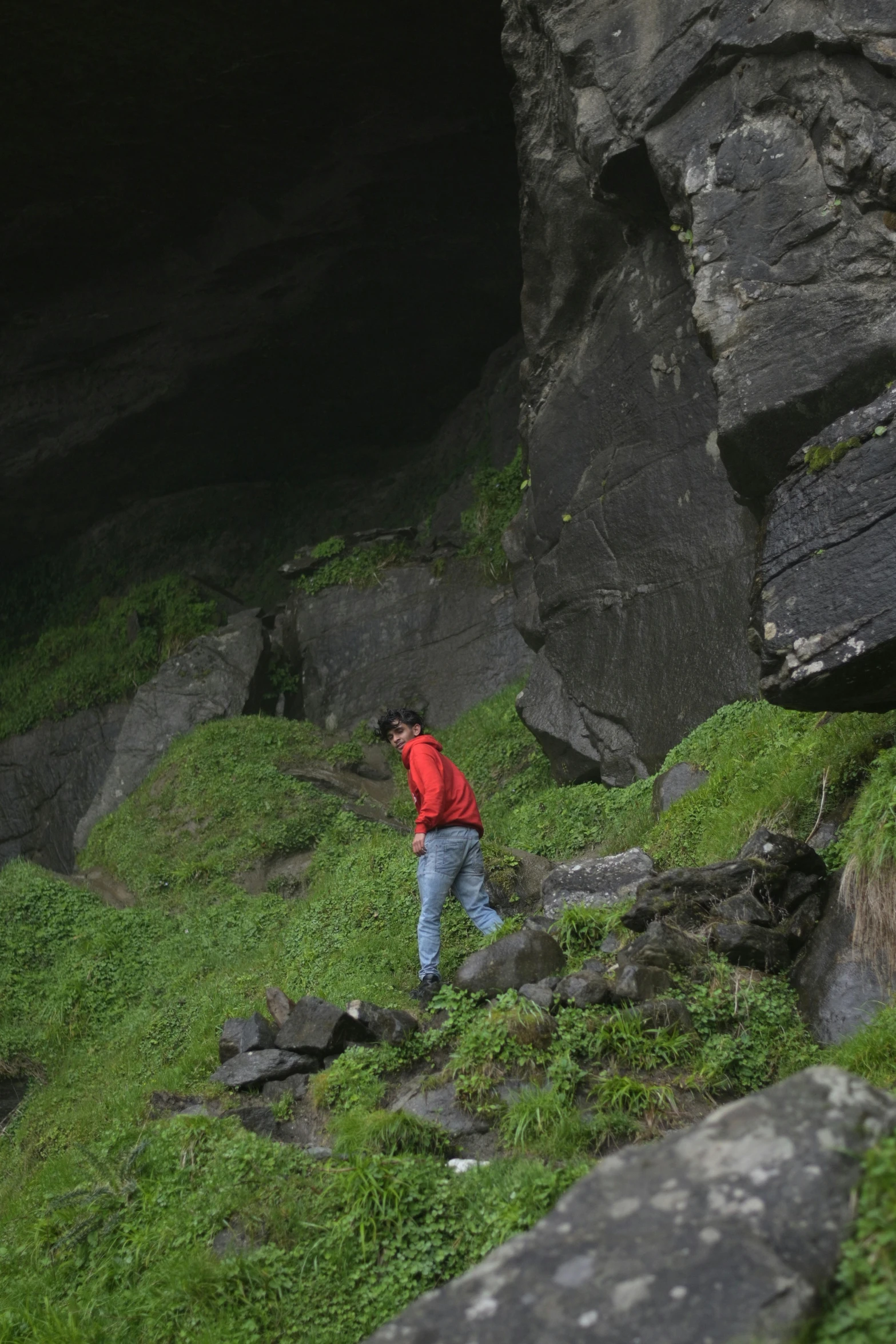 a man in red jacket climbing up steep green hillside