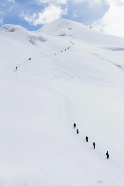 a group of people walking up the side of a mountain on skis