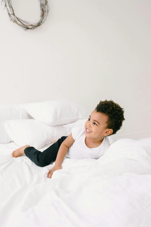 an adorable little boy lays on the sheets in a bed