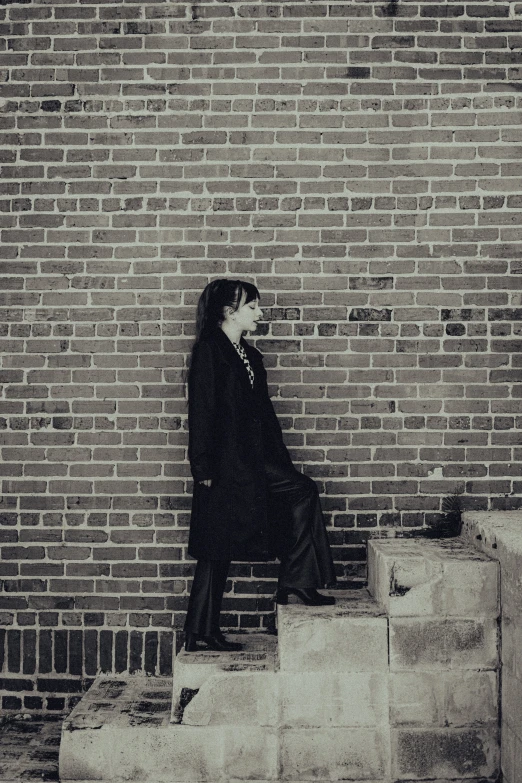 a man in suit and tie standing against brick wall