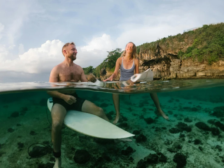 a man and woman sitting in water while holding their surfboards