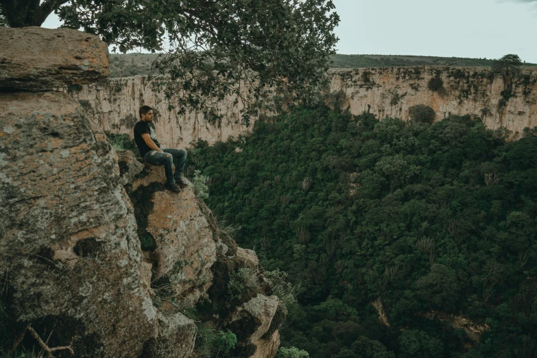 man sits on the edge of a large cliff