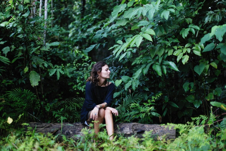 a woman sits on a log in the forest