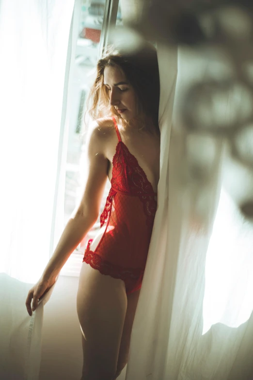 a woman in a red  - top is posing by a window