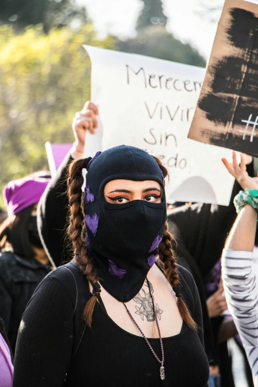 a person wearing a mask with her hands up holding a sign