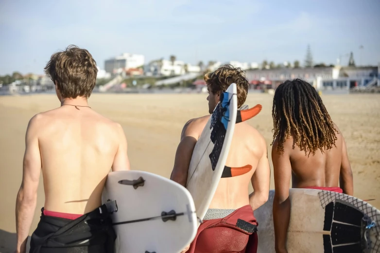 three young surfers are headed down the beach and look at the ocean