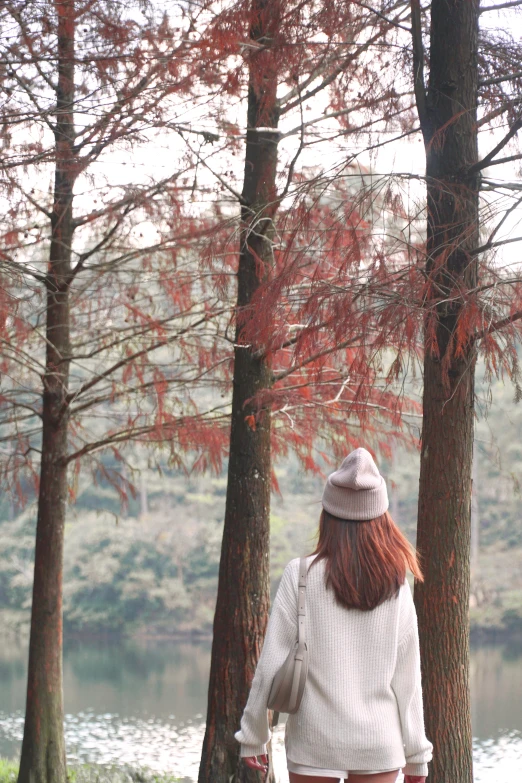 a young woman wearing a white cardigan walks in the woods