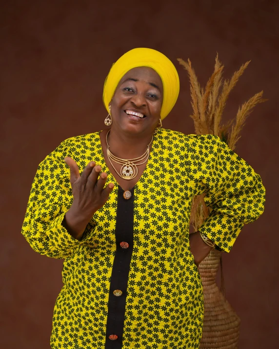 a woman with a bright yellow dress smiling and holding her hands together in front of a vase