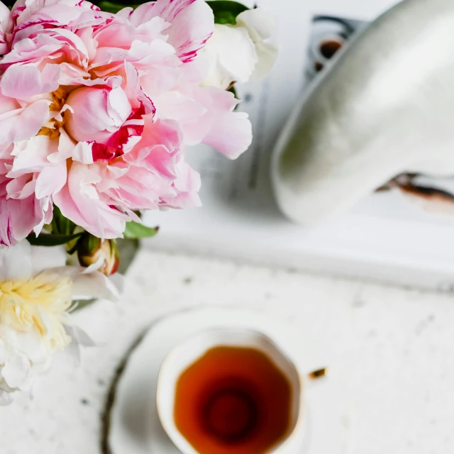 pink flowers are on a table next to a tea cup