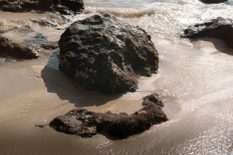 two rocks are in the sand near water