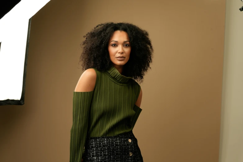 a woman with curly hair in a sweater is standing in front of a wall