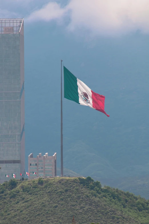 the flag of mexico waving on top of a hill