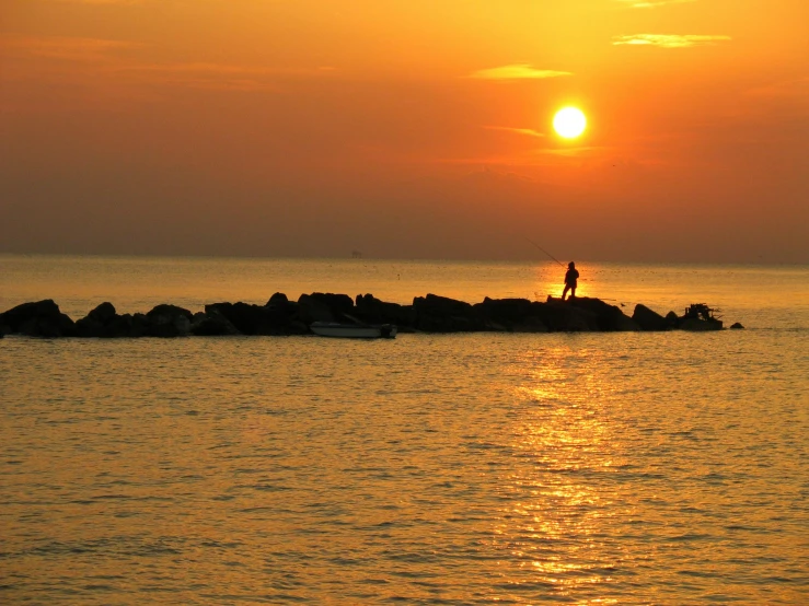 man standing on a small rocky outcropping by the ocean at sunset