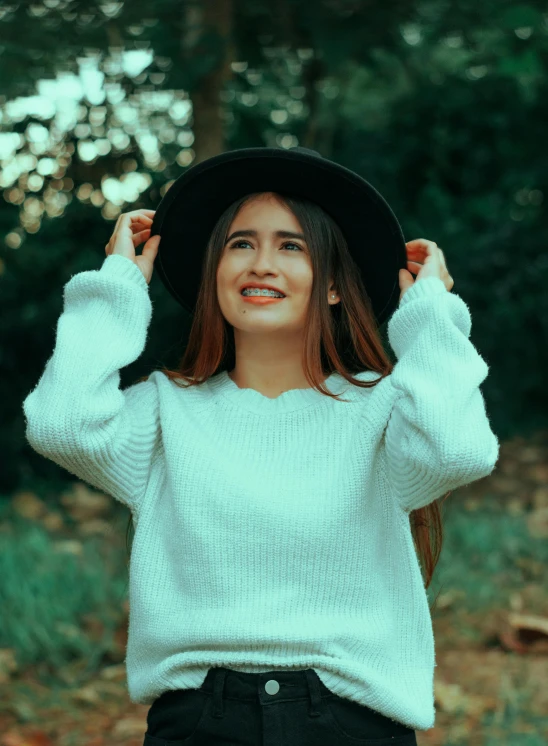 a beautiful young woman standing in the woods with her arms behind her head