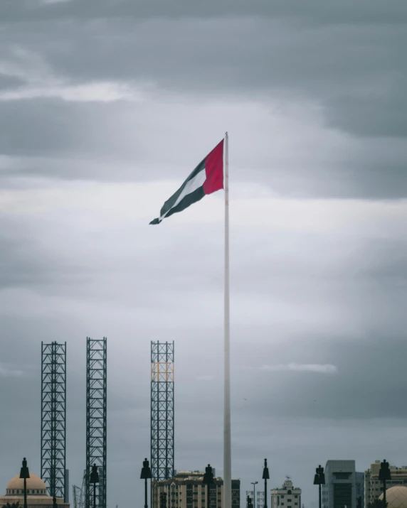 the red and white flag is high in the cloudy sky