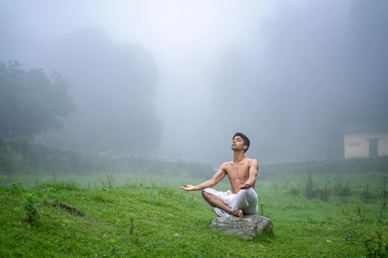 a man sitting in the fog on a rock and making yoga