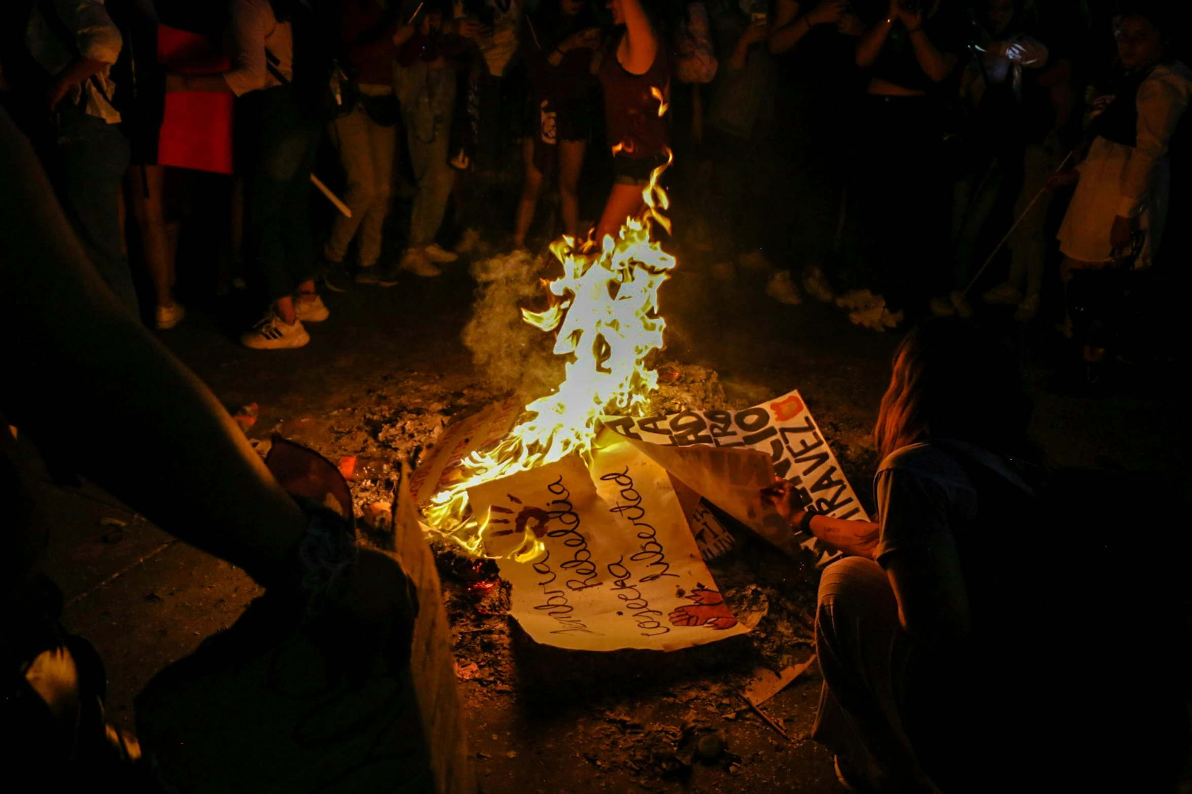 a crowd watches as people light a birthday cake in the dark